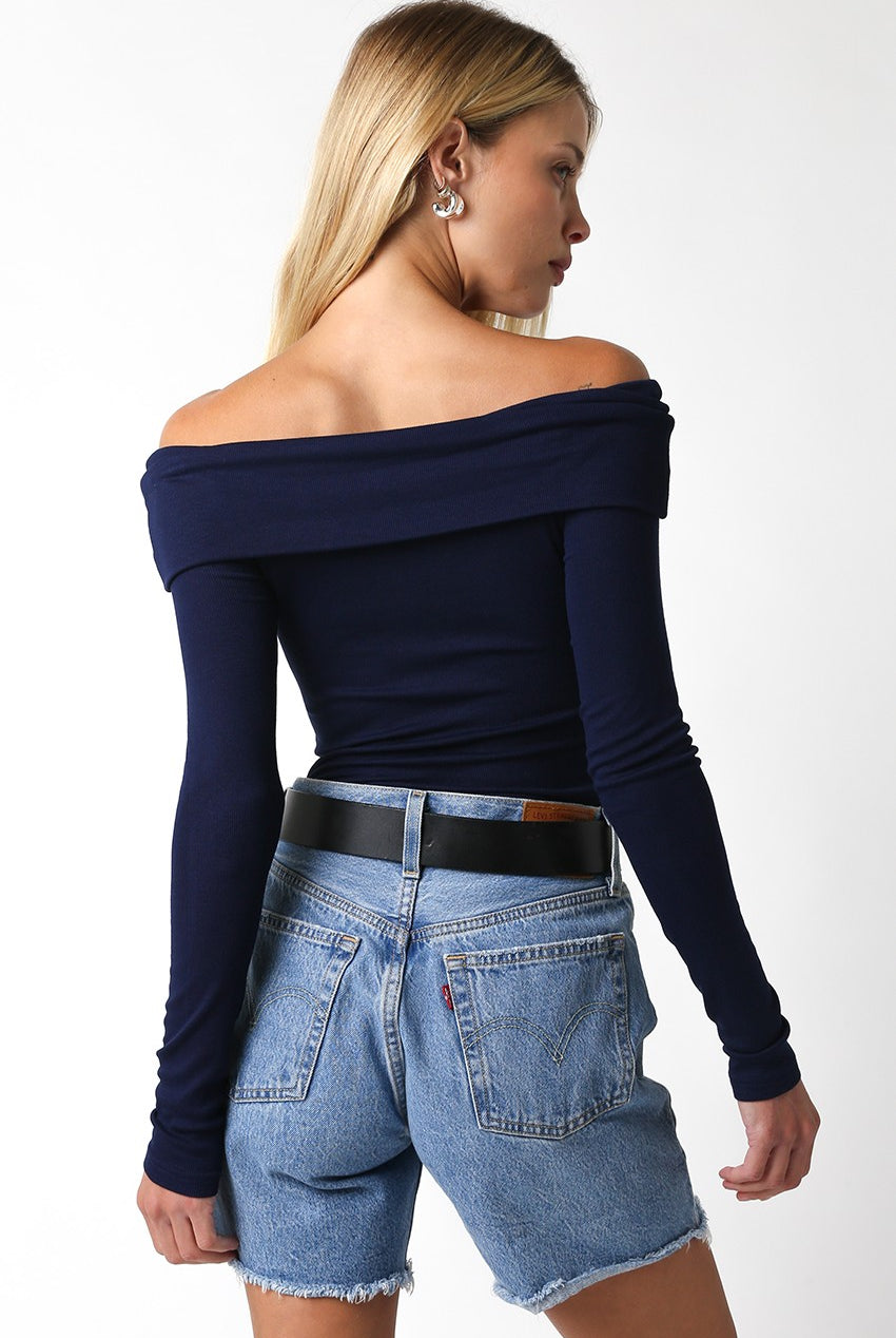 Back View of Woman wearing the Zena Navy Off-Shoulder Top and blue jean shorts.