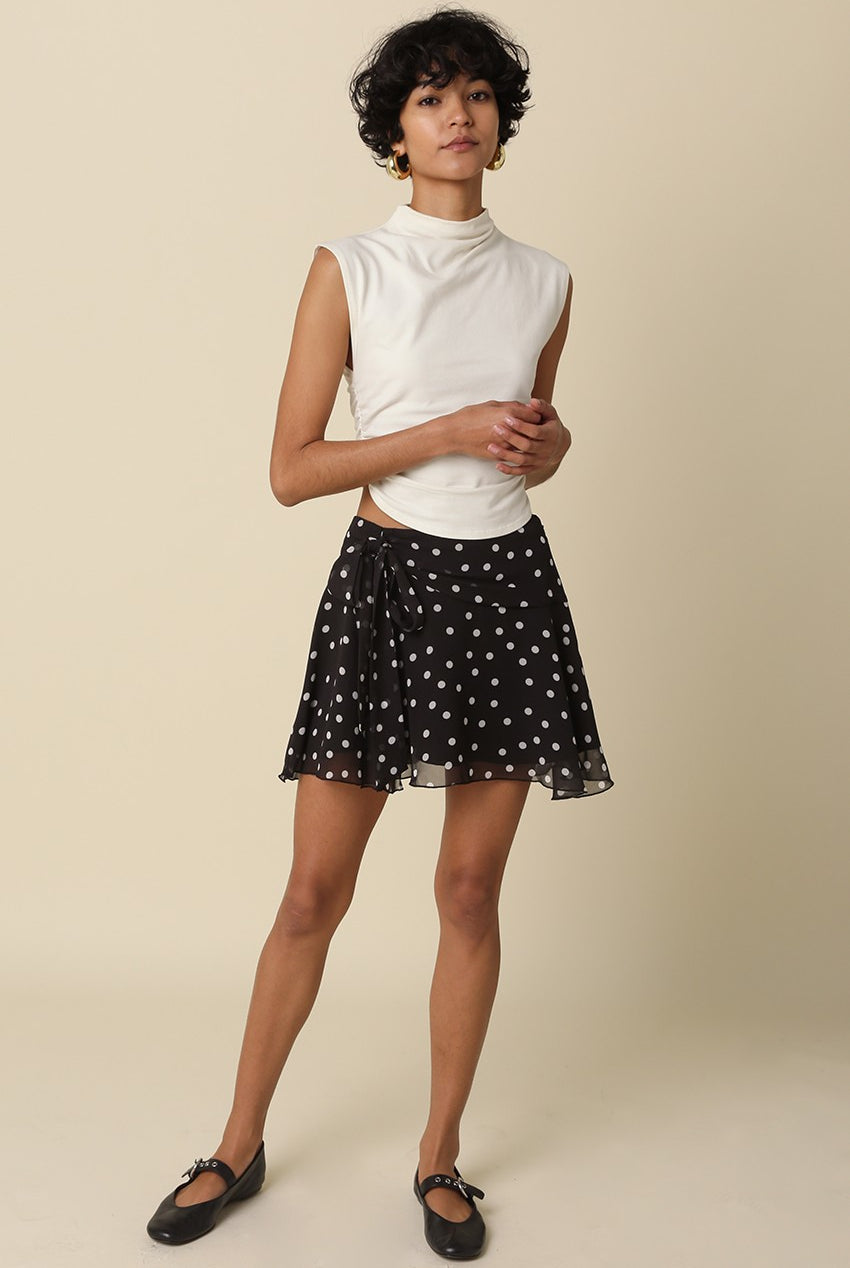 Full body shot of a model styling the Eleni black polka dot ruffle mini skirt with a white sleeveless top