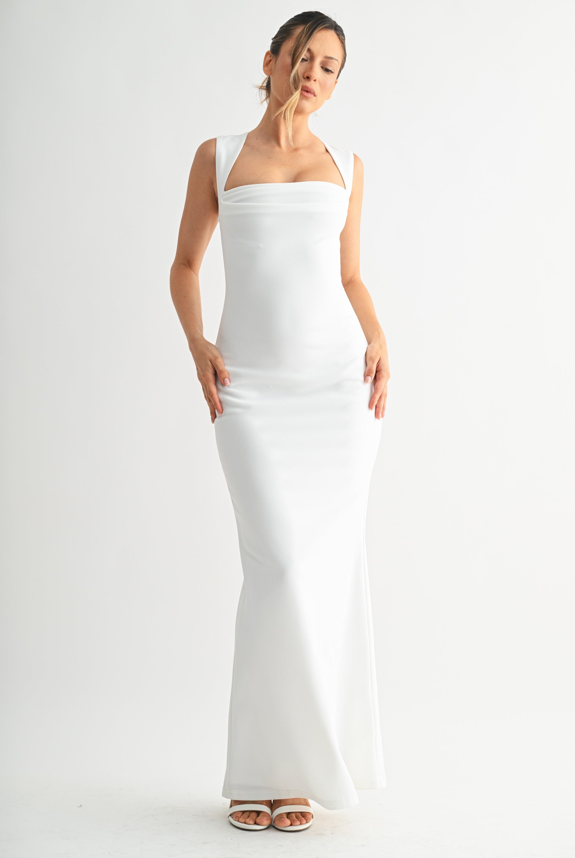 Full length view of a woman wearing a sleek white sleeveless gown with a flared hem