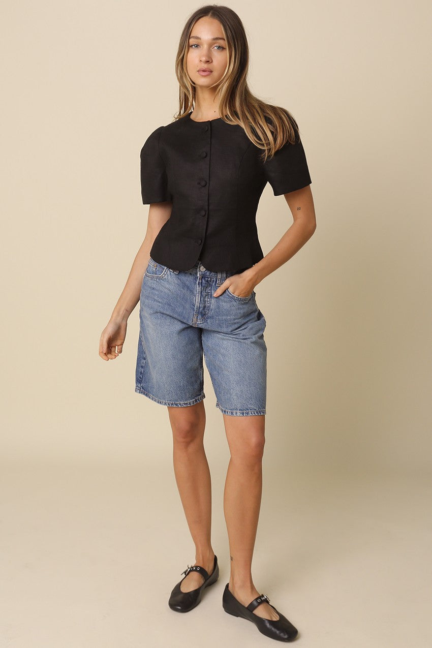 Model wearing a black linen blouse with puff sleeves and button front closure.