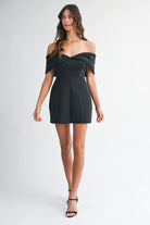 Shot of the black off-the-shoulder dress styled with strappy white heels