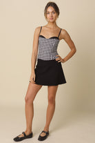 Matea black and white plaid fitted corset top featuring adjustable straps and peekaboo bra detail.