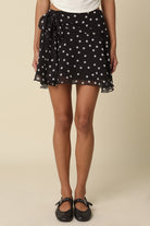 Close-up front view of the Eleni black and white polka dot ruffle mini skirt showing the draped tie detail