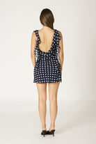 Close-up back view of a navy and white polka dot dress showcasing the ruffle design and flirty mini length