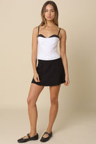 Full body view of the lingerie-inspired Devyn white corset top styled with a black mini skirt